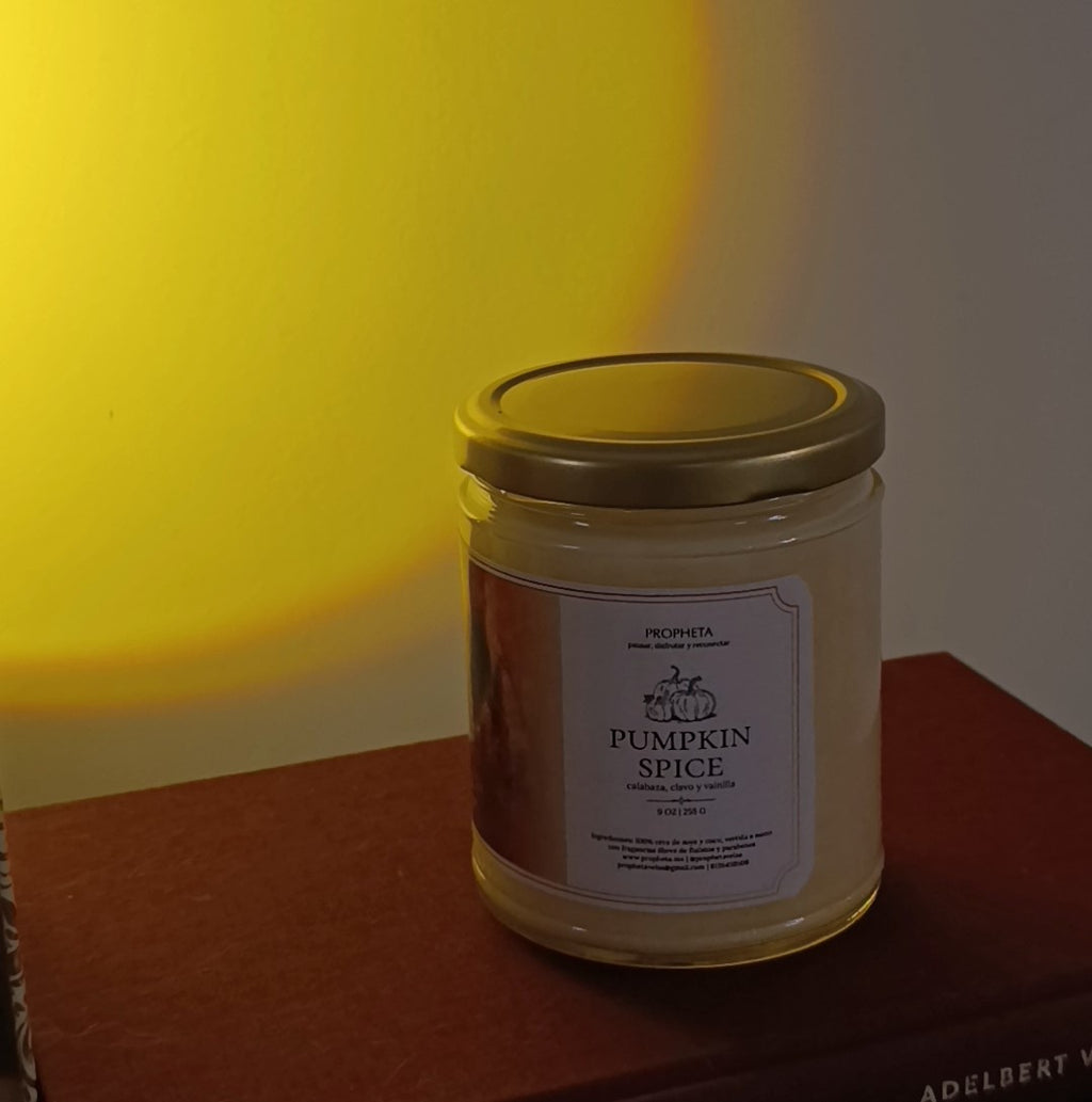 vela aromática pumpkin spice con libros y luz cálida de fondo